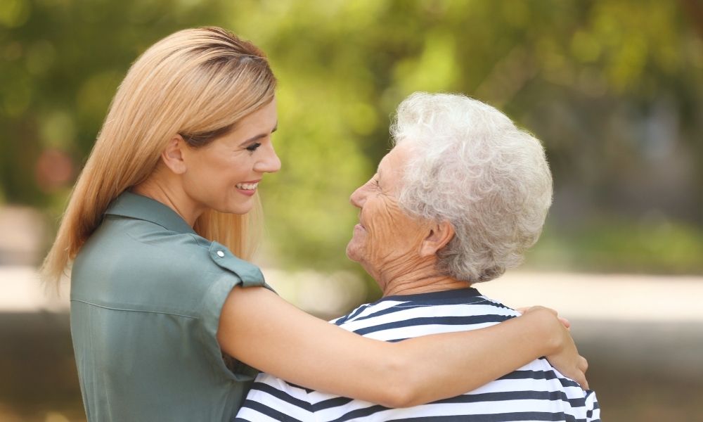 A caregiver embraces a smiling older woman outdoors.
