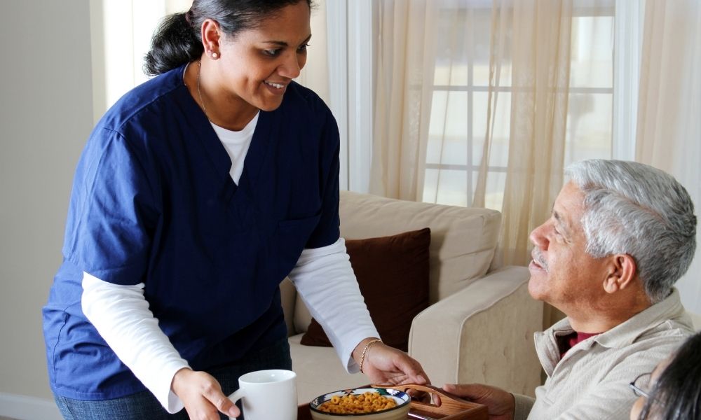 A caregiver serves a meal to an older man seated at a table.
