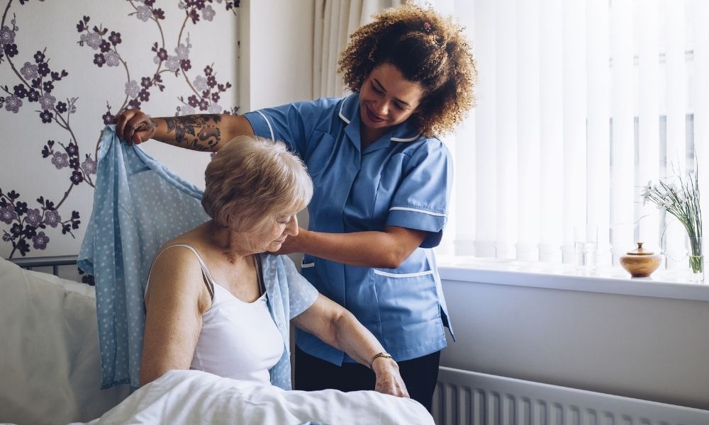 A caregiver gently combs an older woman’s hair.