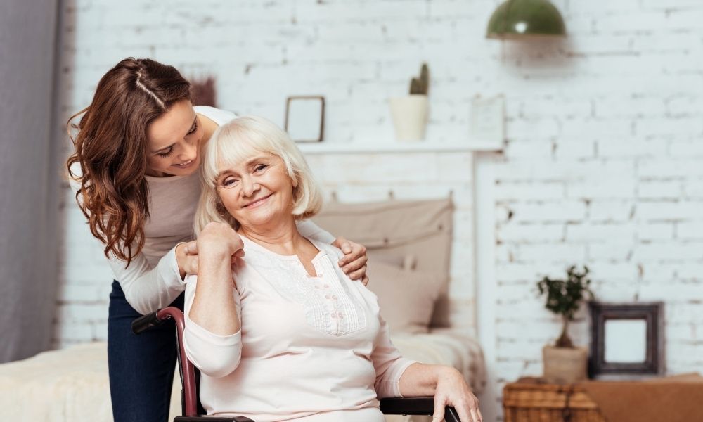 An adult daughter hugs her smiling older mother at home.